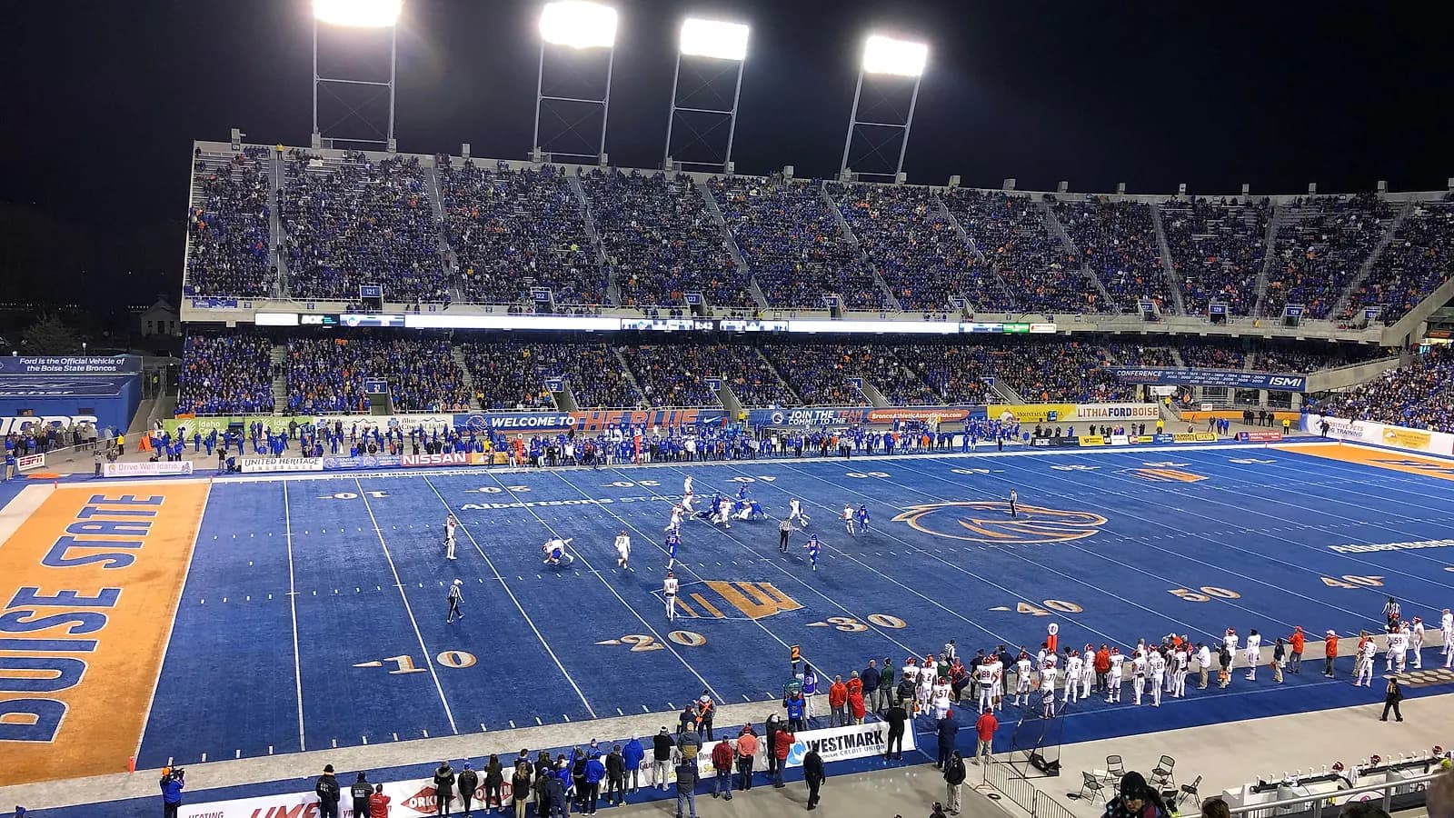 Wide game-night view across Albertsons Stadium's blue field and main grandstand in Boise.