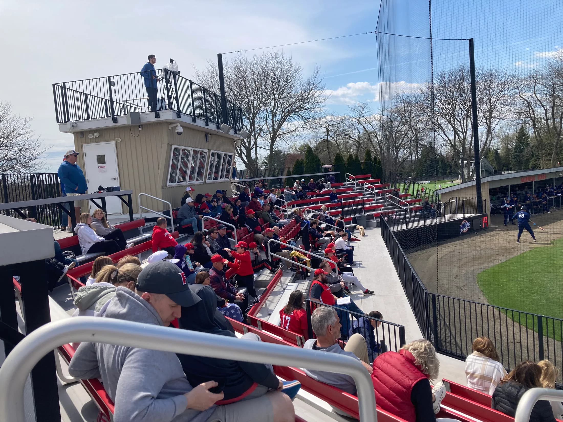 Cook Field’s occupied bleachers, seatback rows, aisle railings, protective netting and press box in Paul Baker’s Stadium Journey collection. This is an actual spectator-area view, without an exact capture date or numbered camera seat; compare the present event’s assignment.