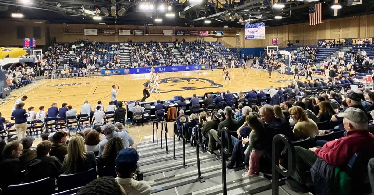 Bank of Colorado Arena’s basketball court, surrounding seating and stepped aisle in Ben Alkaly’s Stadium Journey photograph. Nearby spectators and aisle railings affect this angle. The August 2025 article date is not an independently verified capture date or a section-and-row seat identification.