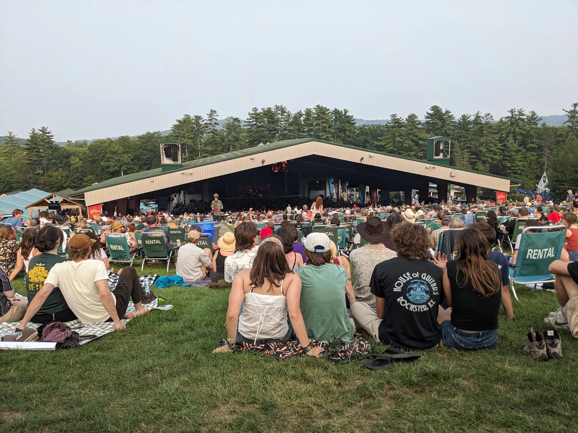 Wide audience view across BankNH Pavilion toward its covered stage, seating areas, and lawn crowd in Gilford.