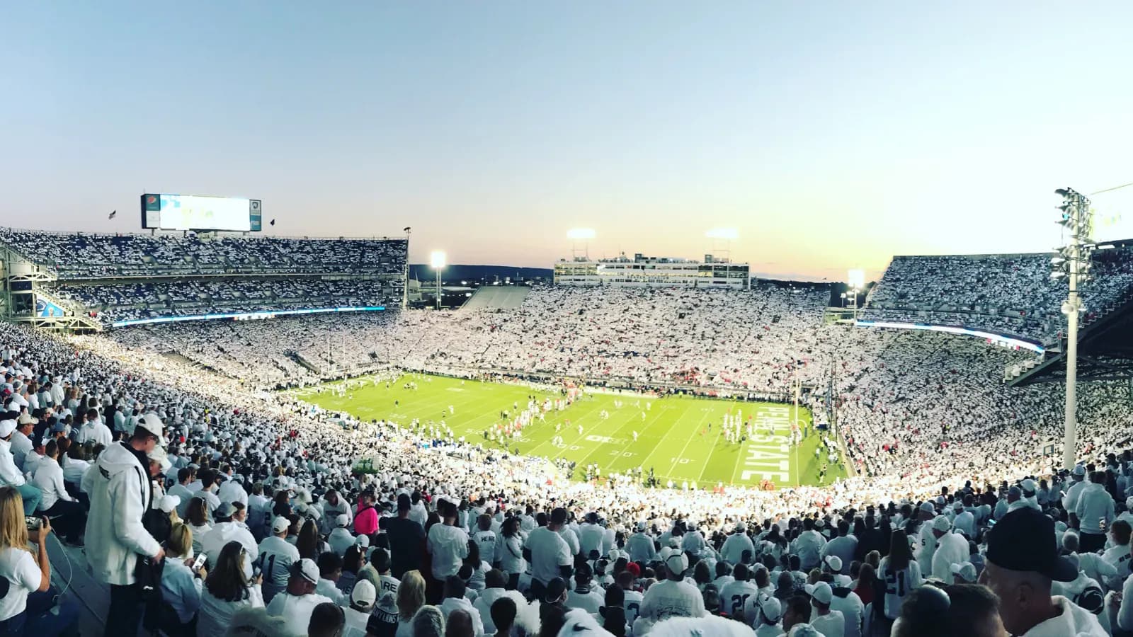 Wide White Out game view across Beaver Stadium's field and packed seating bowl at sunset.