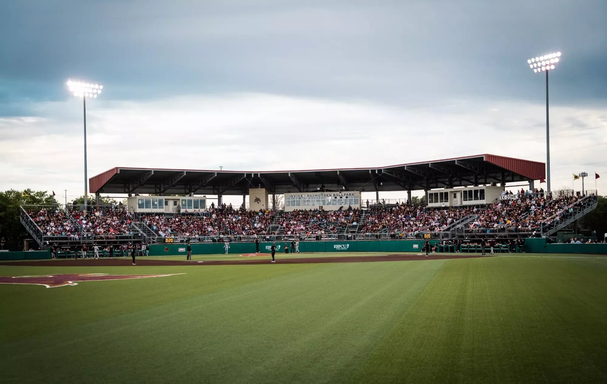 Irvine–Rasmussen Ballpark’s occupied covered grandstand seen from across the field during Texas State’s April 7, 2026 game against Texas A&M, as identified in the official gallery. This field-side camera position does not imply spectator access to the playing surface. No numbered camera seat is supplied.