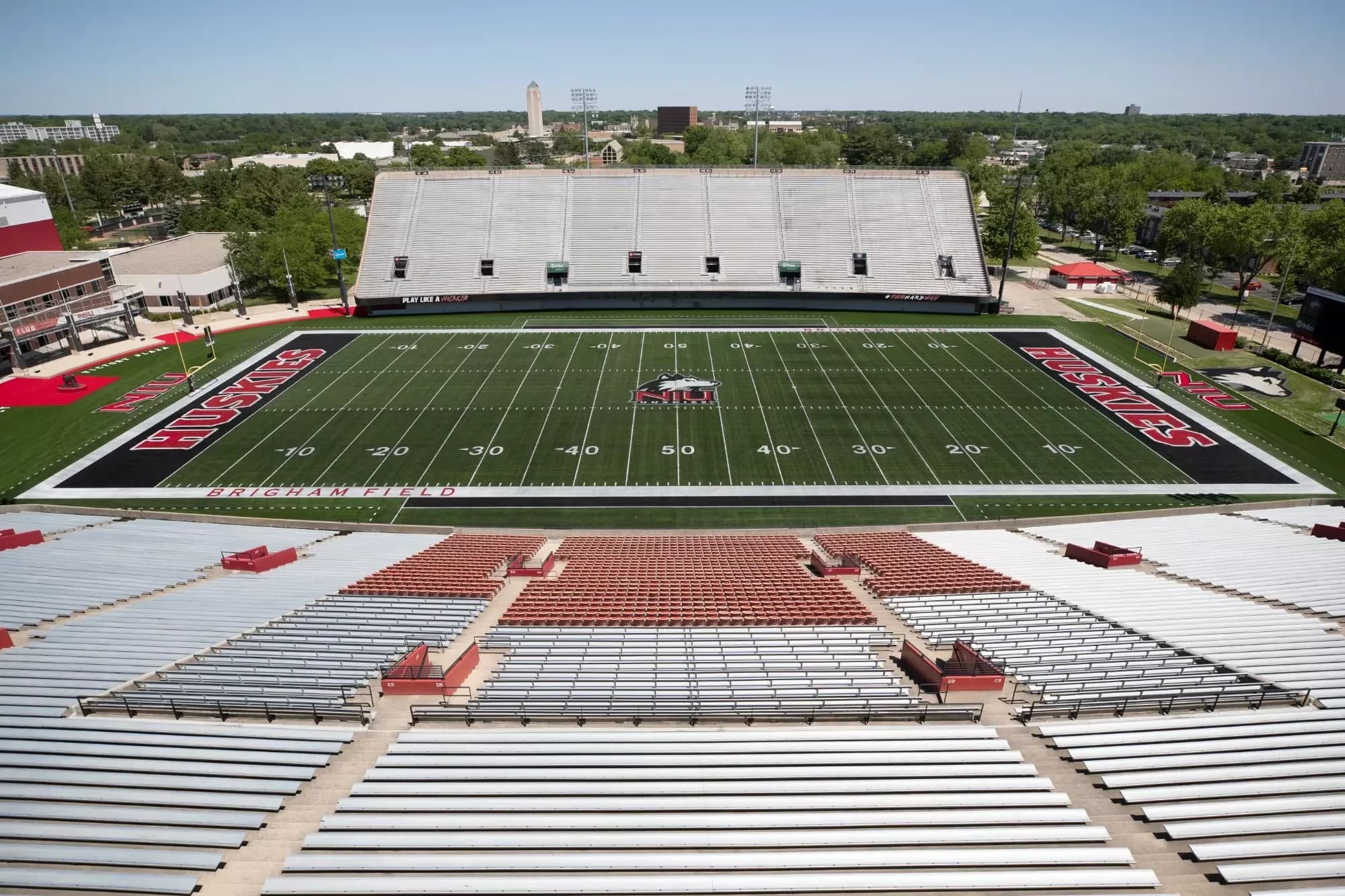 Elevated view across Brigham Field and Huskie Stadium’s sideline grandstands, showing bleachers and the central chairback block. The owner labels this as its 2024 new-turf photograph; it is not a numbered-seat view.