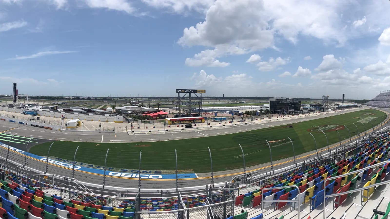 Panoramic view across Daytona International Speedway's frontstretch, infield, and multicolored grandstands.