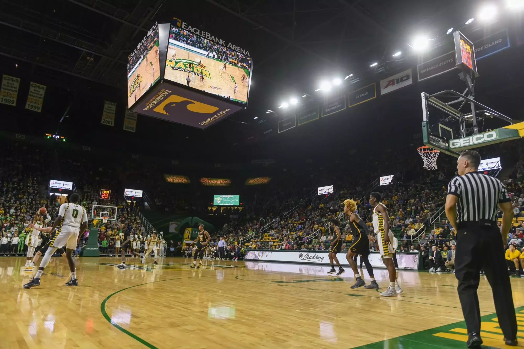 EagleBank Arena’s basketball court and nearby seats from a baseline position, with players and an official in the foreground. George Mason’s facility gallery supplies this older reference without a confirmed capture date or exact seat; floor branding and event arrangements can change.
