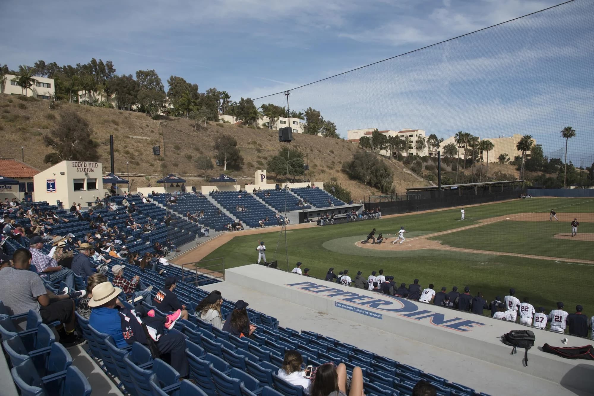 Eddy D. Field Stadium’s blue seating and press box seen across the diamond from a different angle in Pepperdine Athletics’ earlier-season facility collection. Netting and the dugout roof remain visible. The source supplies no numbered spectator camera seat or exact capture date.
