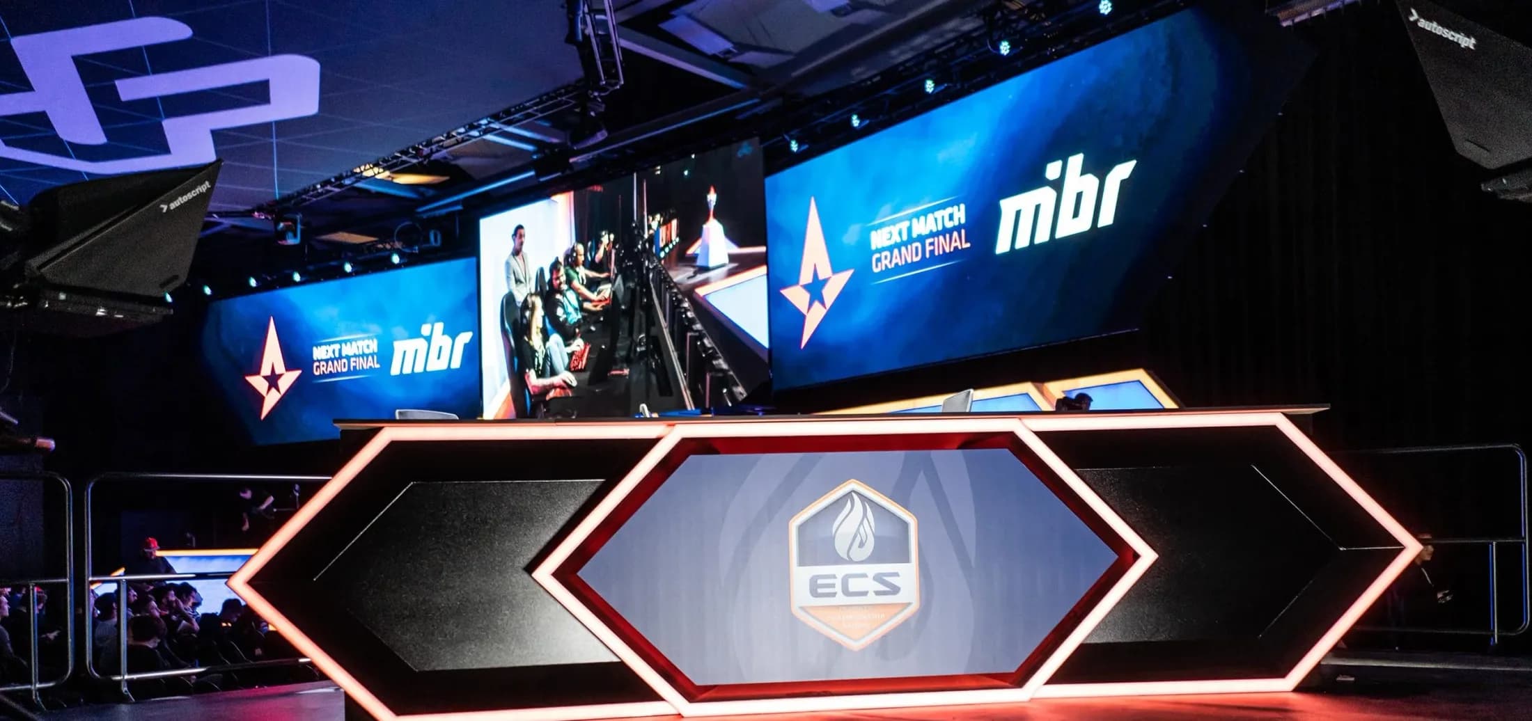 The broadcast desk, competition stage and large screens inside Esports Stadium Arlington, from the builder’s project gallery. This is an undated project photograph of an esports configuration; wrestling-ring layouts, seating and sightlines can differ by event.