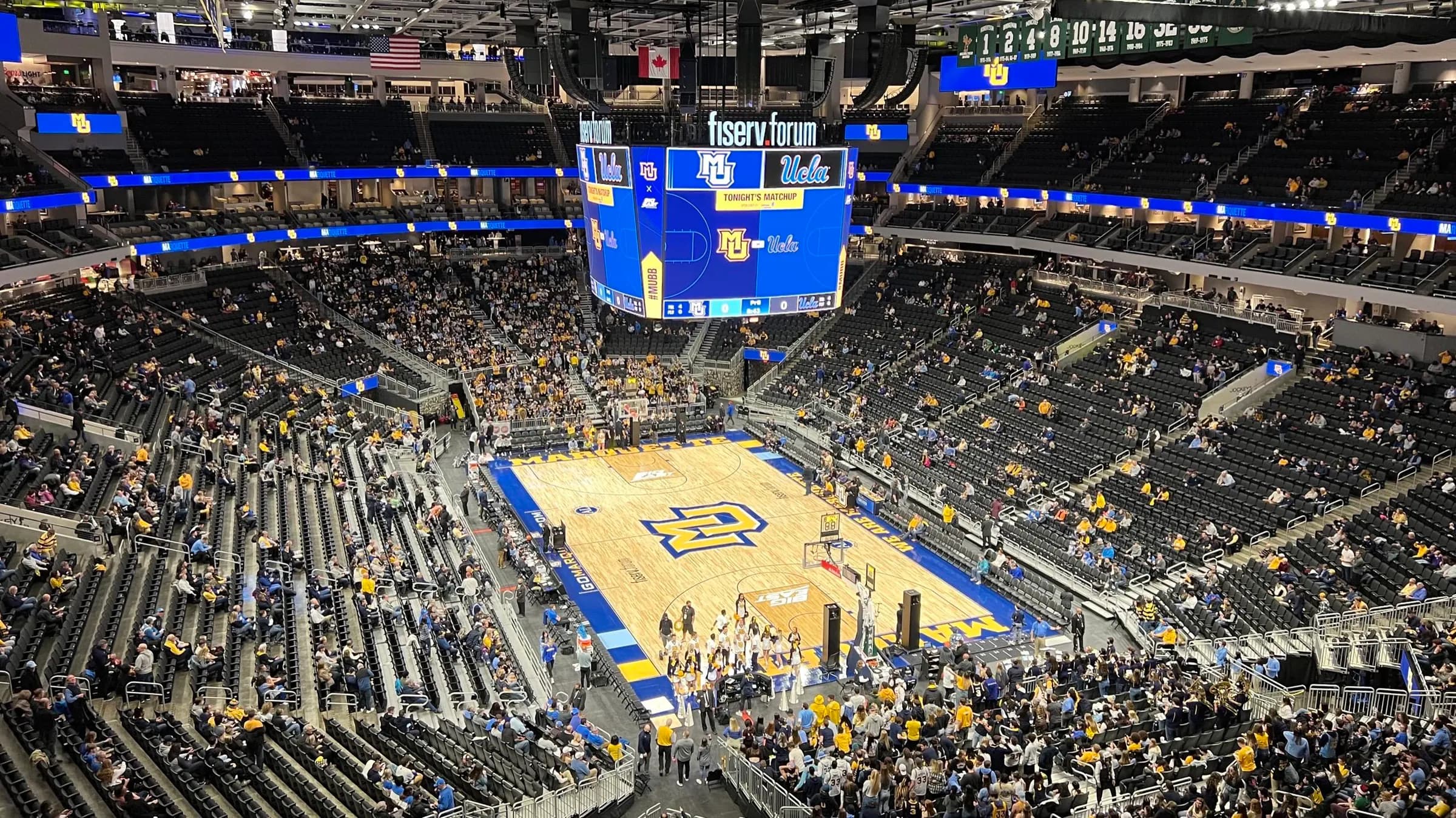 Upper-level view across the court, scoreboard, crowd, and seating bowl inside Fiserv Forum.