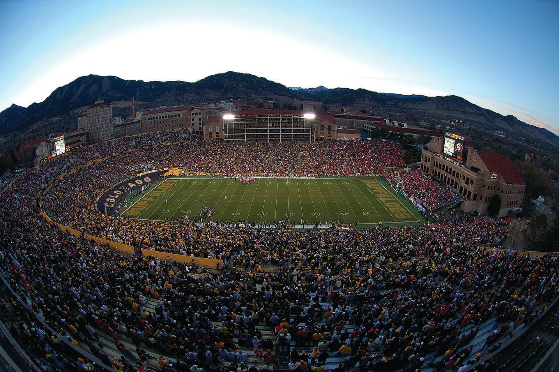 Wide game-day view across Folsom Field's complete football bowl with the Flatirons beyond the stadium.