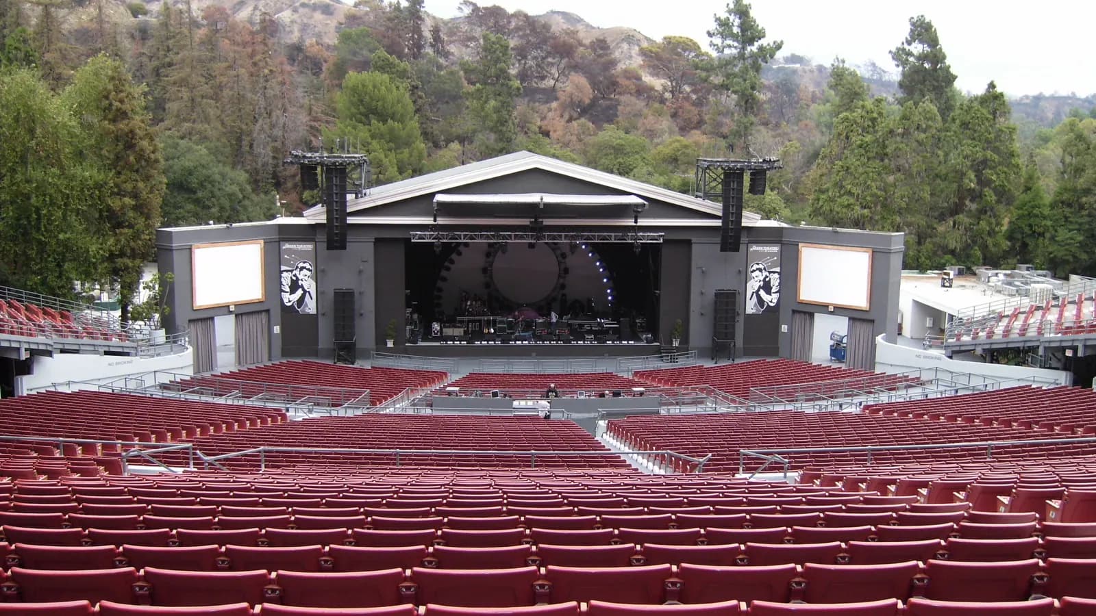 Wide view over the Greek Theatre's seating toward its stage and wooded Griffith Park setting.