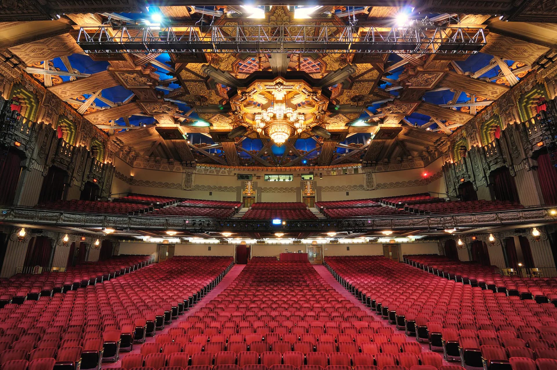 Wide view from the stage across the Hollywood Pantages Theatre auditorium, red seats, balcony, chandelier, and Art Deco ceiling.