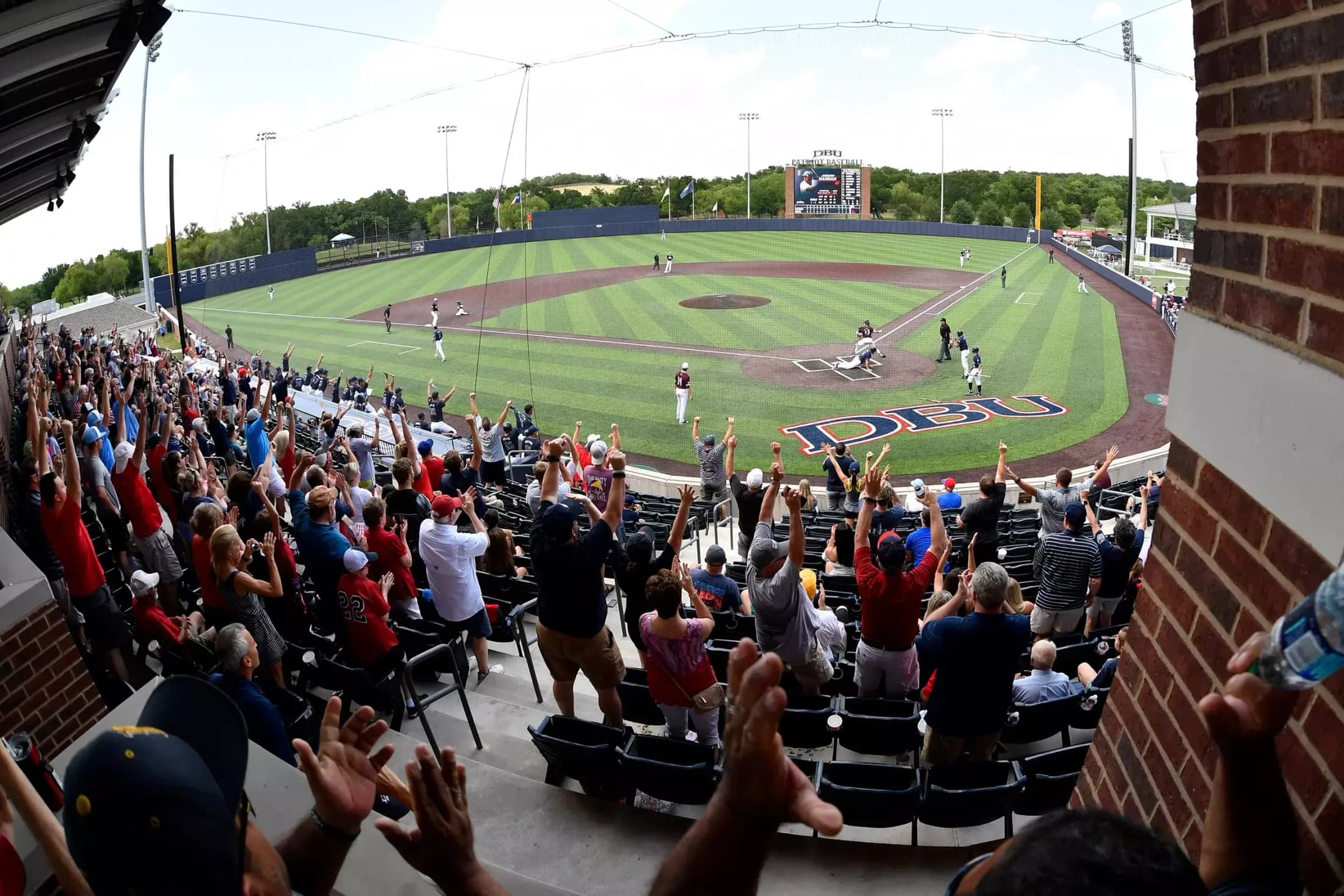 Horner Ballpark’s covered seating and occupied bowl in Dallas Baptist Athletics’ facility collection. The foreground brick support, railing and protective netting remain visible; no individually numbered camera seat or unobstructed-view guarantee is supplied.