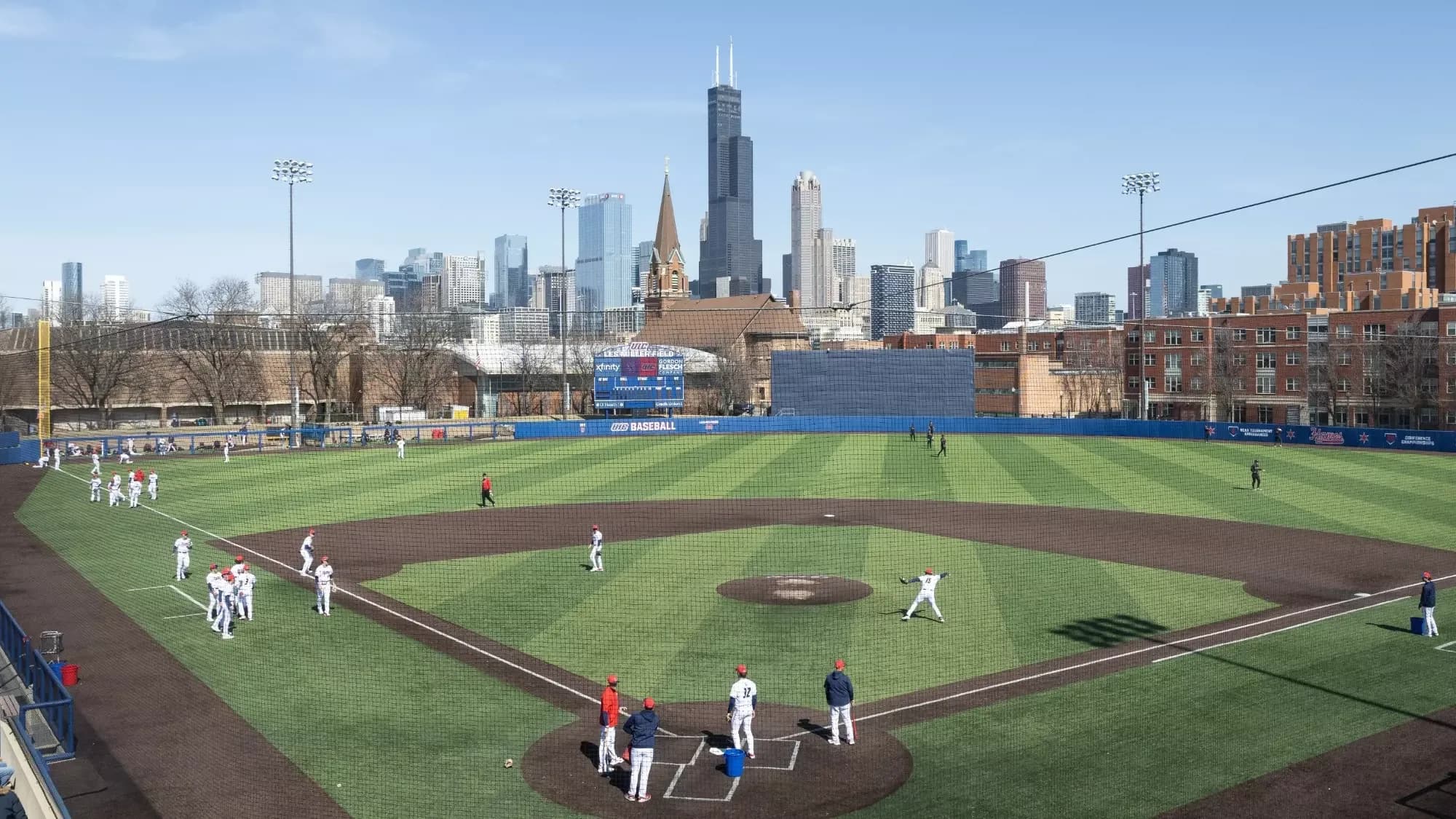 Curtis Granderson Stadium’s diamond and Chicago skyline during on-field introductions in UIC Athletics’ official facility collection. Nearby spectators, railing and protective netting remain visible; the photograph does not imply spectator field access or identify a numbered camera seat or exact capture date.