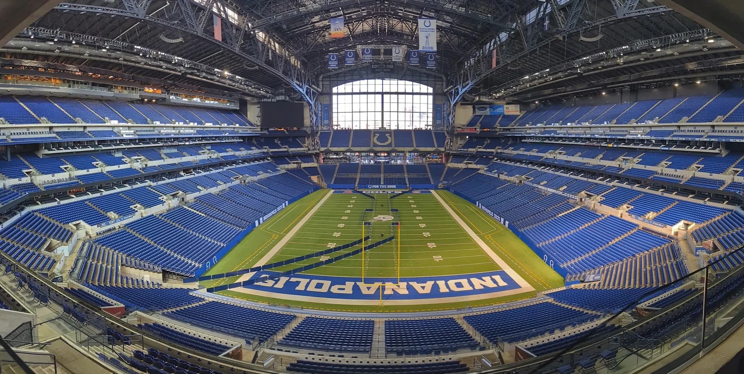Super-wide centered view across the complete Lucas Oil Stadium field, seating bowl, roof, and north window.