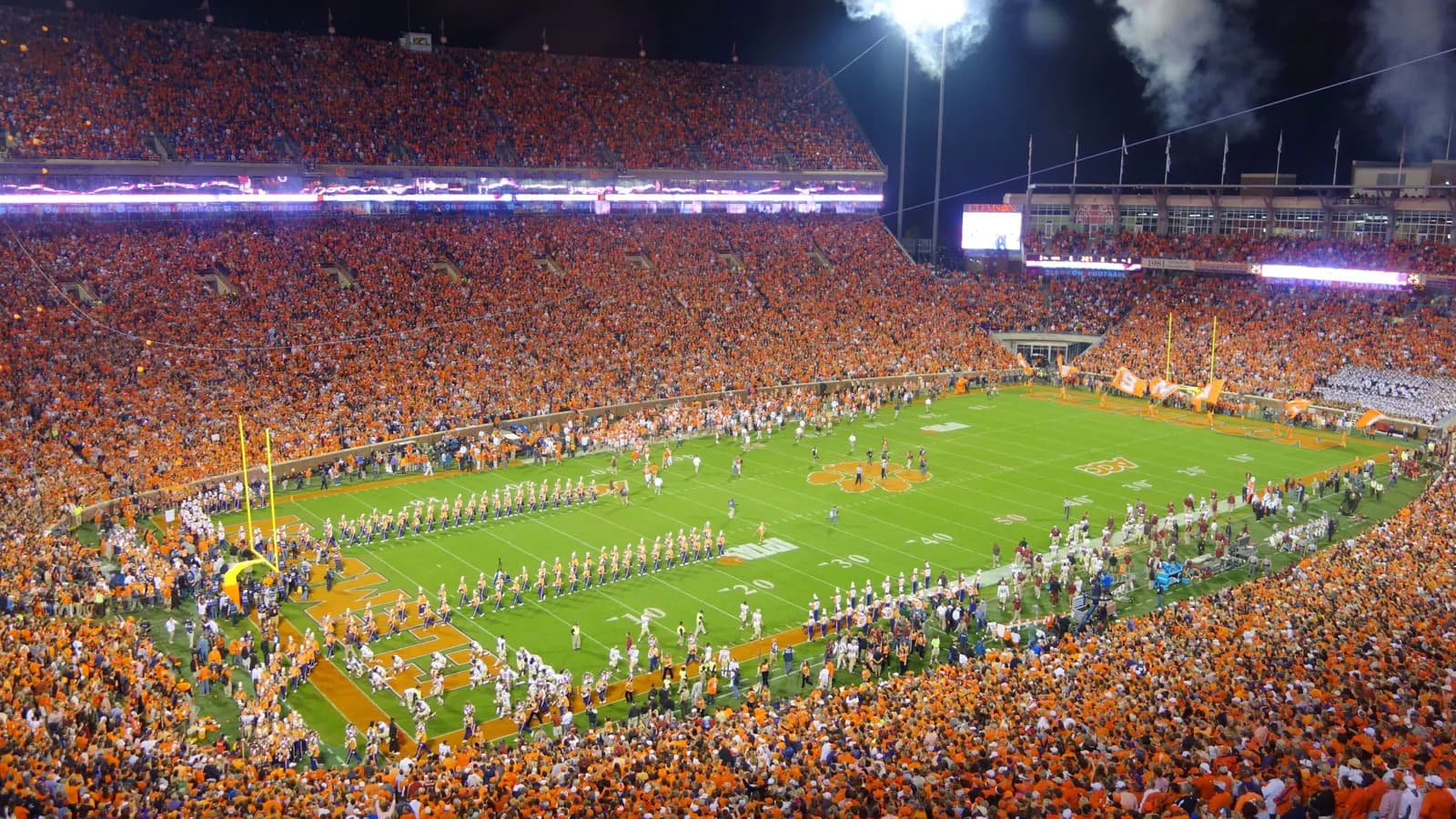 Packed night-game view across Clemson Memorial Stadium's field and orange seating bowl.