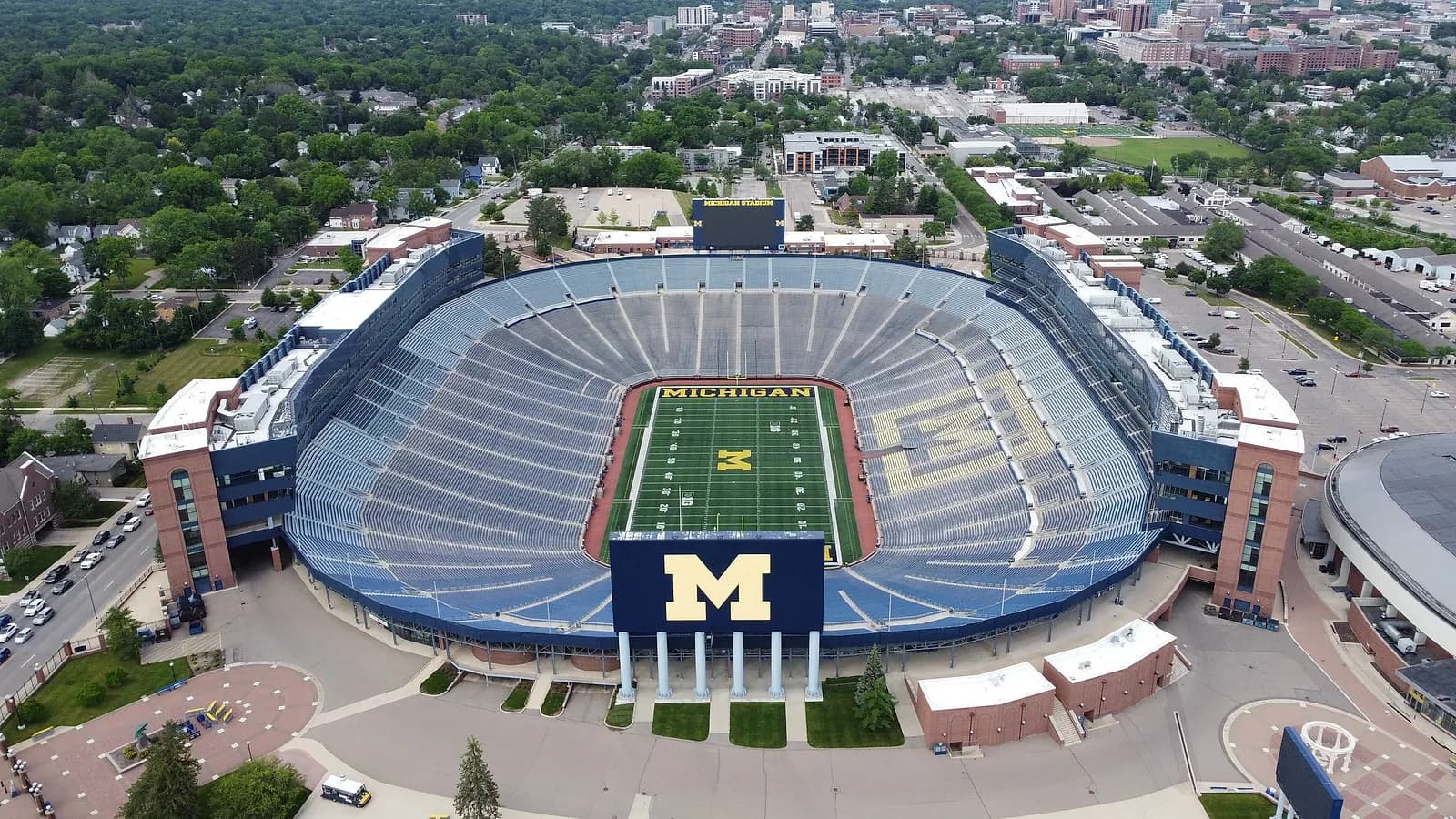 High aerial view of Michigan Stadium, its full seating bowl, and the surrounding Ann Arbor campus.