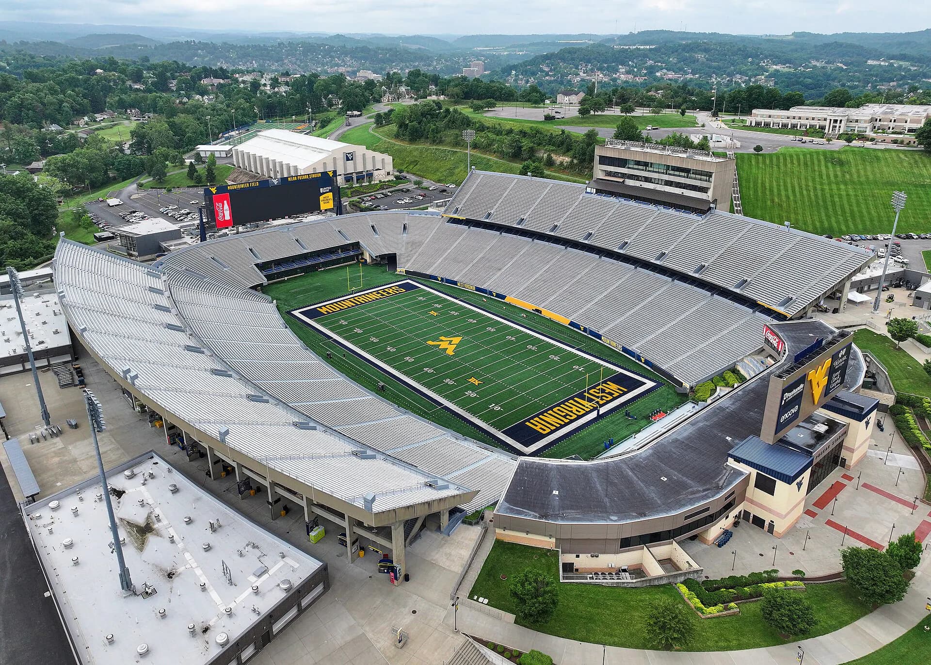 High aerial view into Milan Puskar Stadium showing the complete football field, seating bowl, and arrival context.