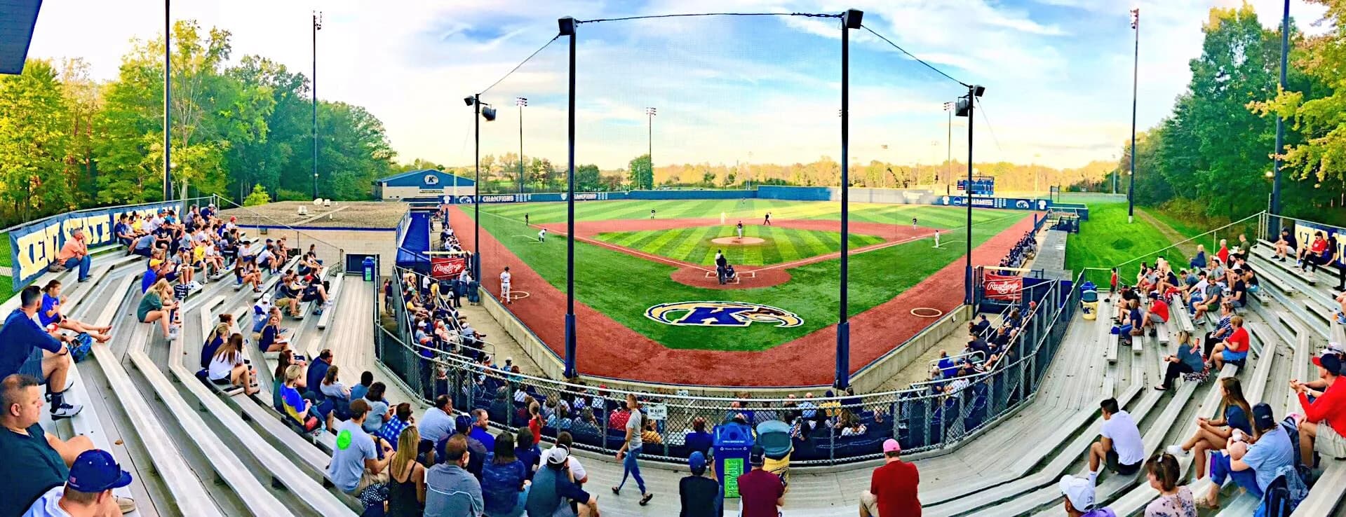 Schoonover Stadium’s occupied grandstand and diamond through protective netting in Kent State Athletics’ older facility collection. Preserve the wide panorama when comparing the seating and netting; no exact capture date or numbered camera seat is supplied.