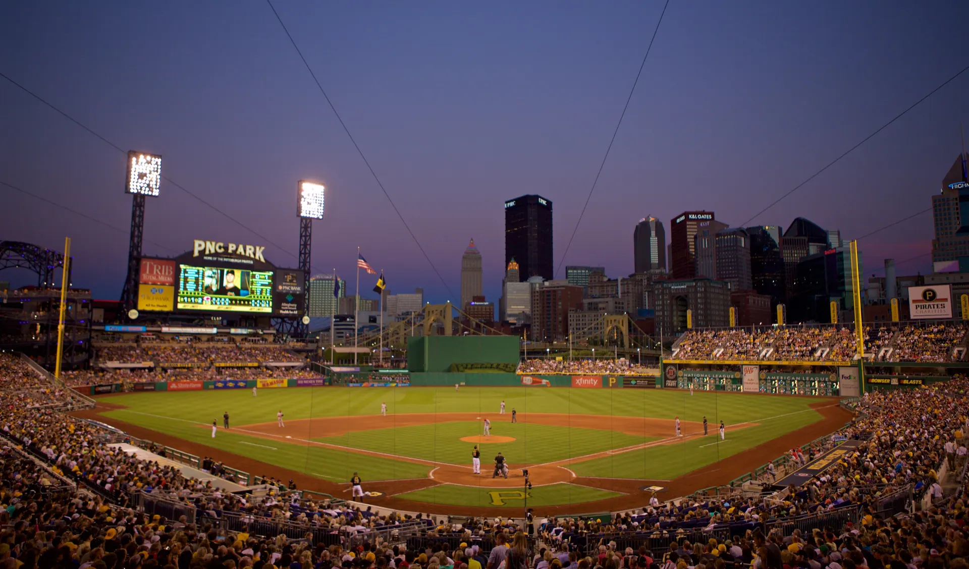 Sharp dusk view from behind home plate across PNC Park's full diamond, seating bowl, and Pittsburgh skyline.