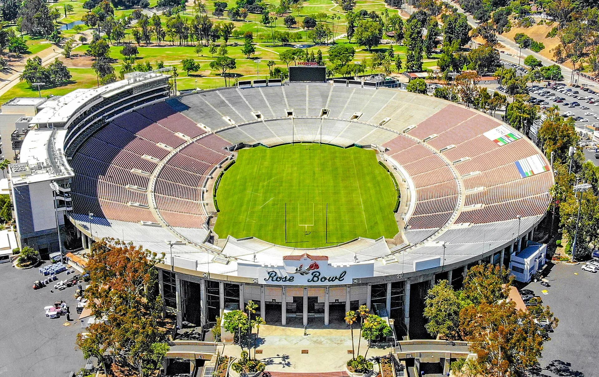 High aerial view into the Rose Bowl Stadium's full seating bowl, field, and surrounding parkland.