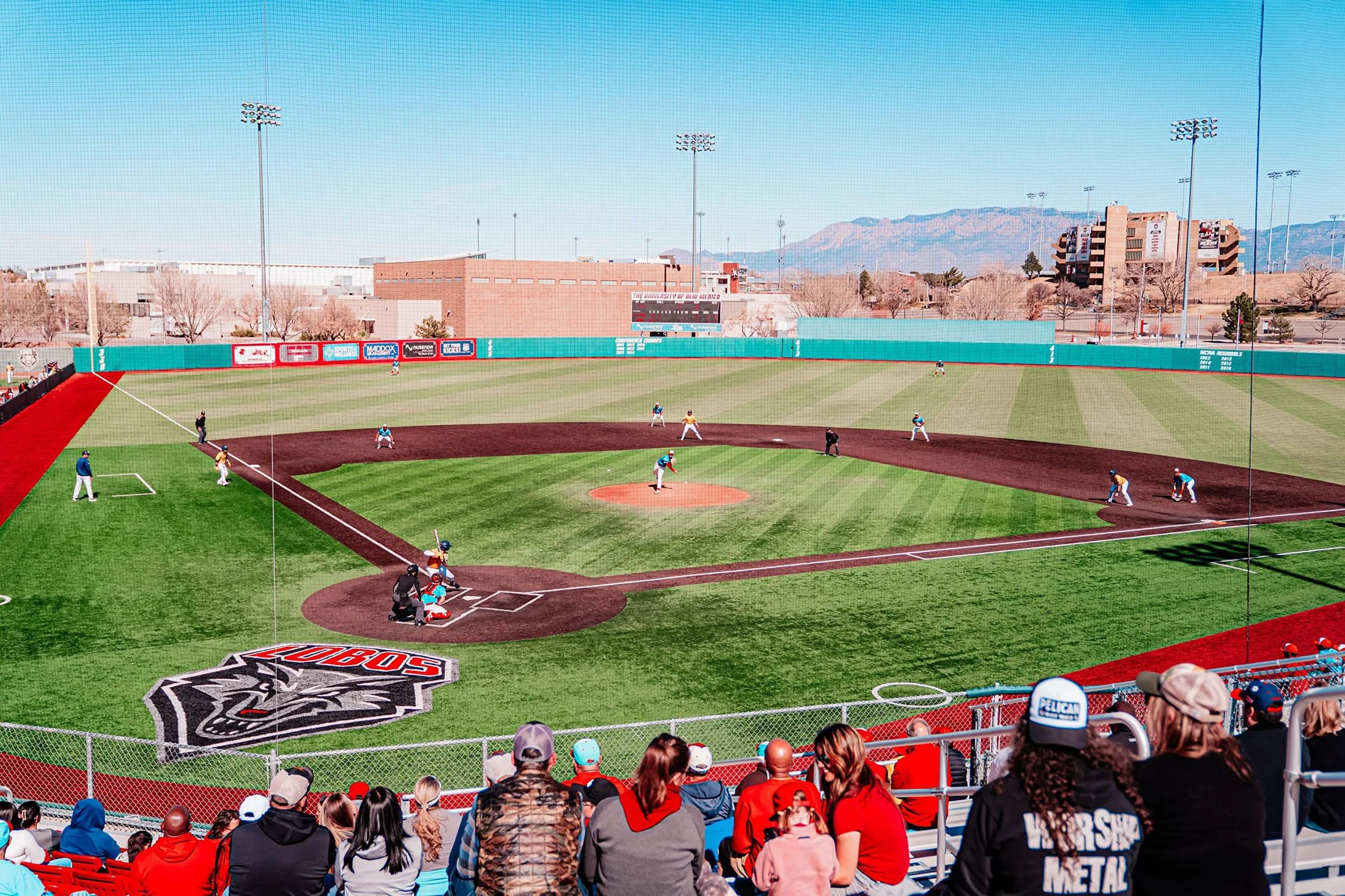New Mexico’s Lobo Baseball Field, also known as Santa Ana Star Field, during a game in the official facility collection. Foreground spectators, protective netting and nearby seats remain visible. No exact capture date or numbered camera seat is supplied; compare the actual game’s conditions.