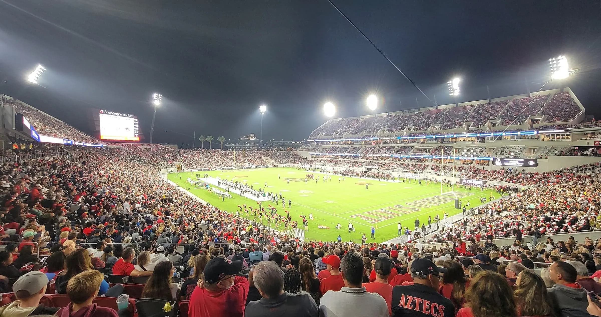 Night panorama across Snapdragon Stadium's field, seating bowl, and video boards.