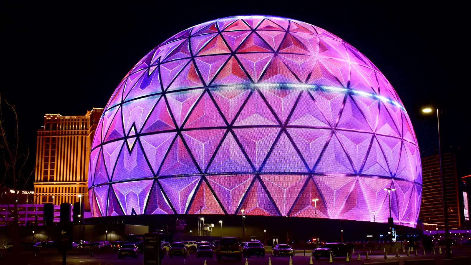 Wide night view of Sphere displaying bright pink and purple geometric graphics in Las Vegas.
