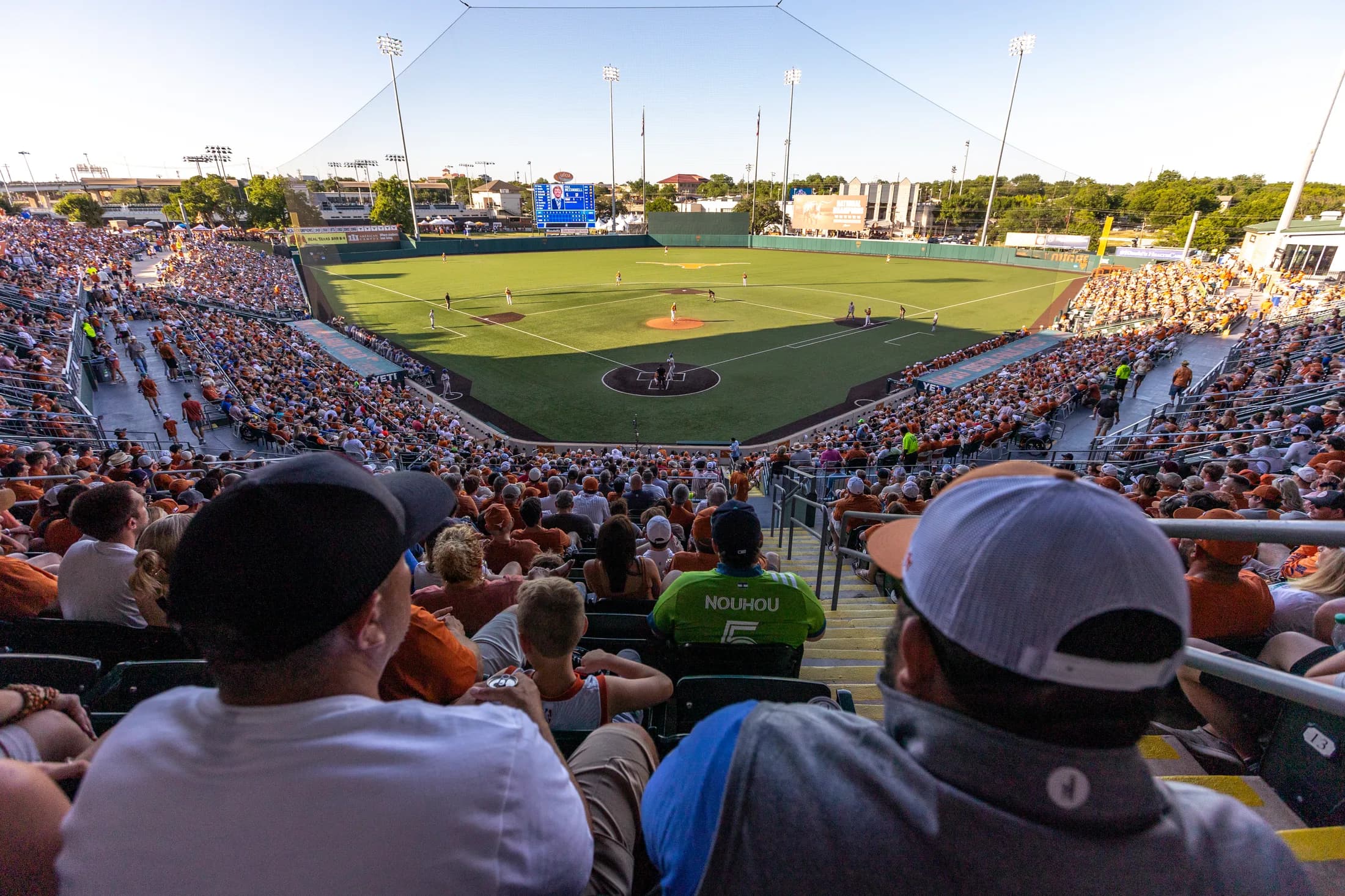 UFCU Disch–Falk Field’s occupied bowl, diamond and outfield during Texas versus Louisiana Tech in the official facility collection. Foreground spectators, protective netting and light poles remain visible. No numbered camera seat or exact capture date is supplied.