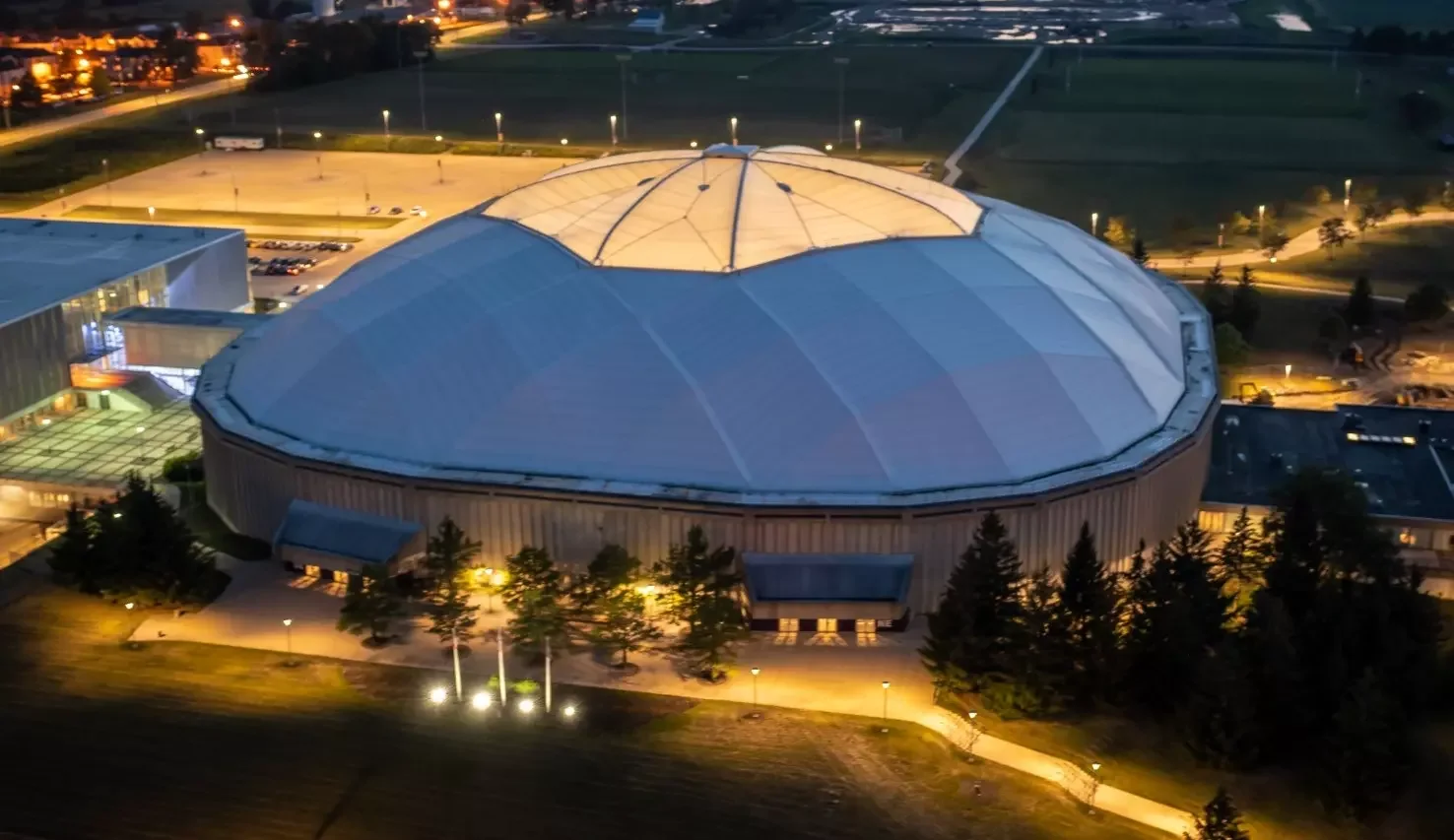 An evening aerial view of the UNI-Dome’s exterior, roof and connected campus facilities, from the current owner facility gallery. The exact capture date is unstated. Use the actual event’s parking and entry instructions for the approach to the building.