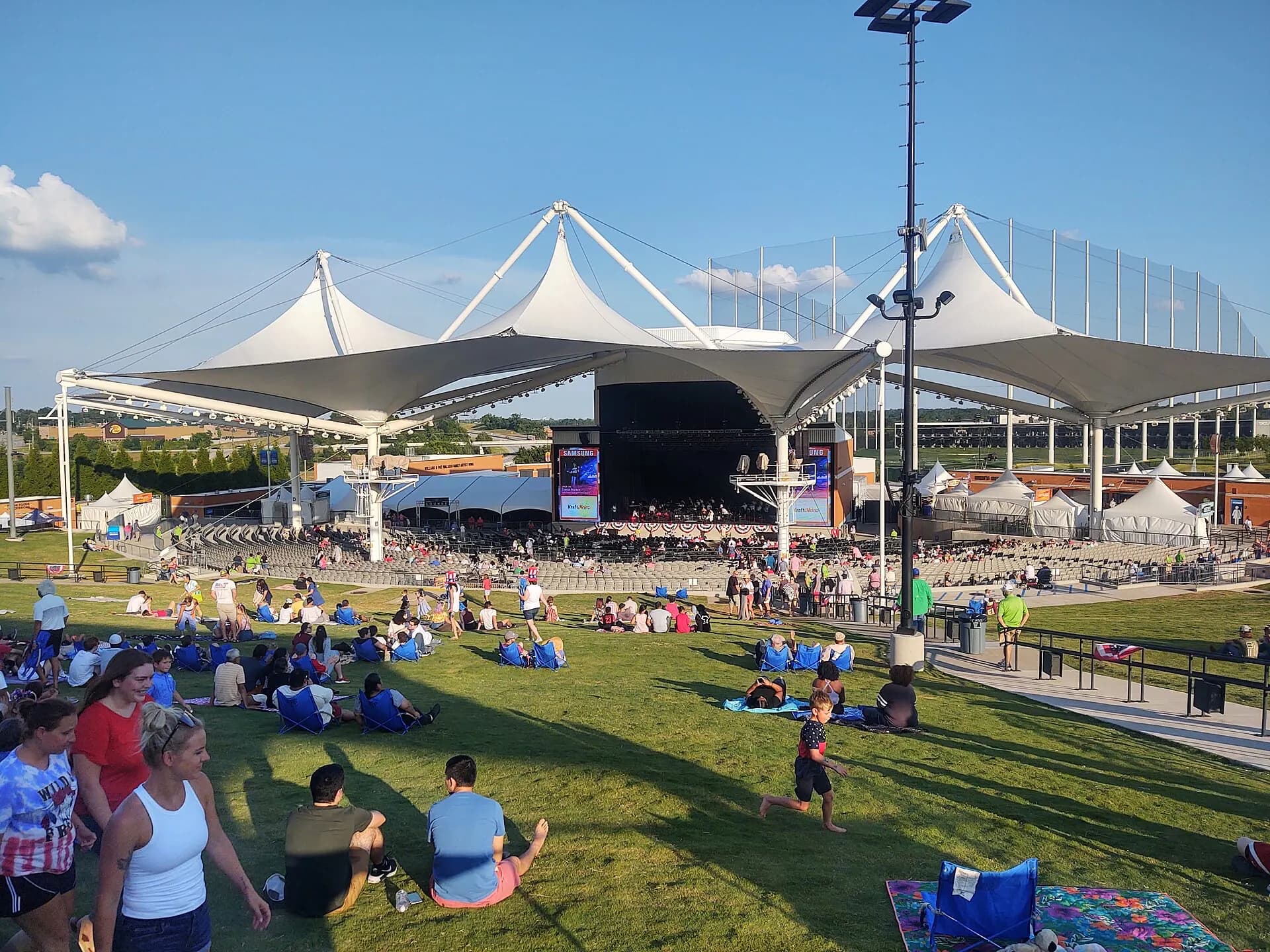 Walmart AMP lawn, covered seating, stage, and audience circulation areas in daylight.