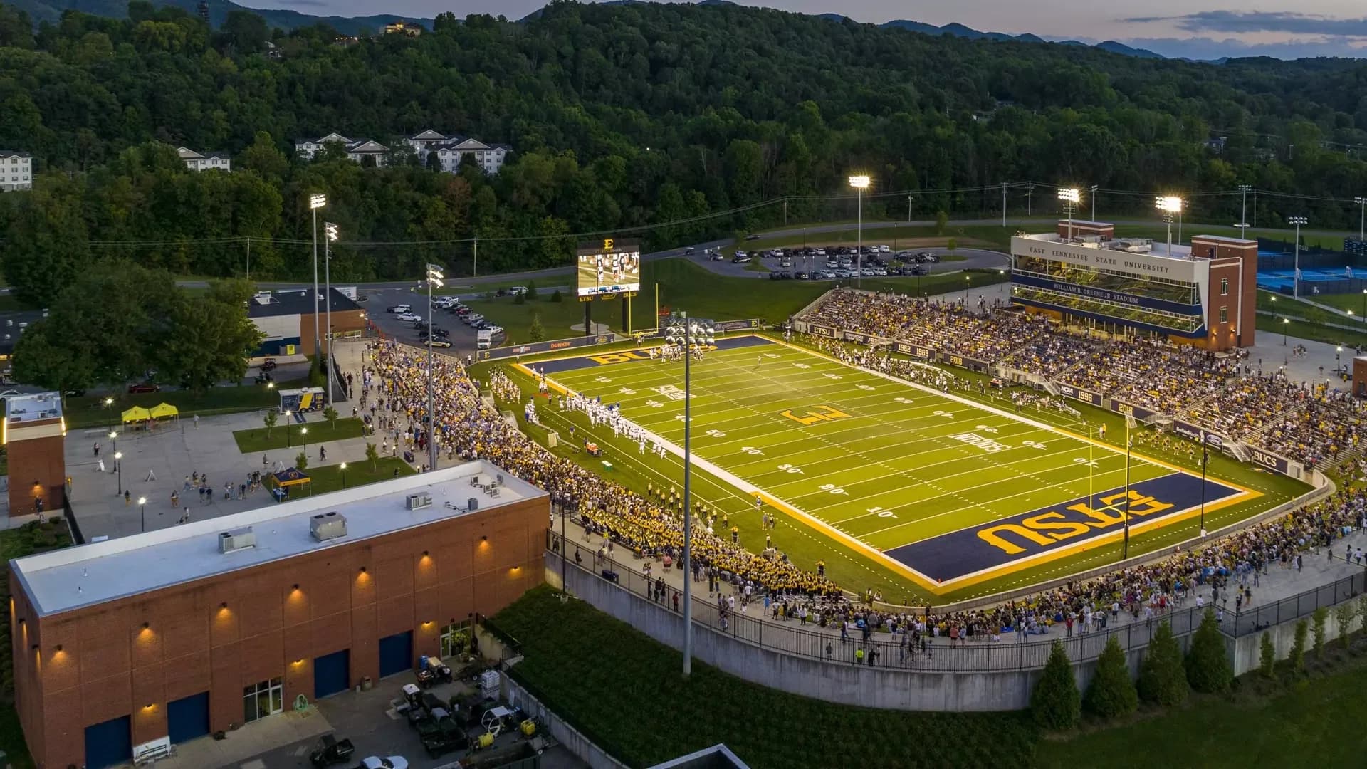 Elevated dusk view of William B. Greene Jr. Stadium, showing both sideline stands, the curved end-zone seating and press-box building. This owner facility photograph was published in its October 2023 image series; exact capture date is unstated. It is an orientation view rather than a numbered-seat sightline.